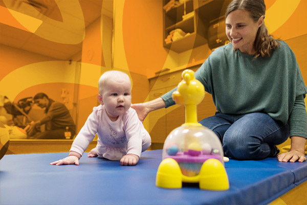 therapist engaging with a baby on a play mat in room