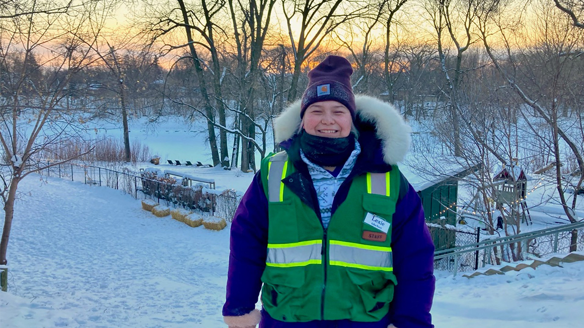 Lexie, dressed in winter clothes, posses for a photo with a sunset in the background.