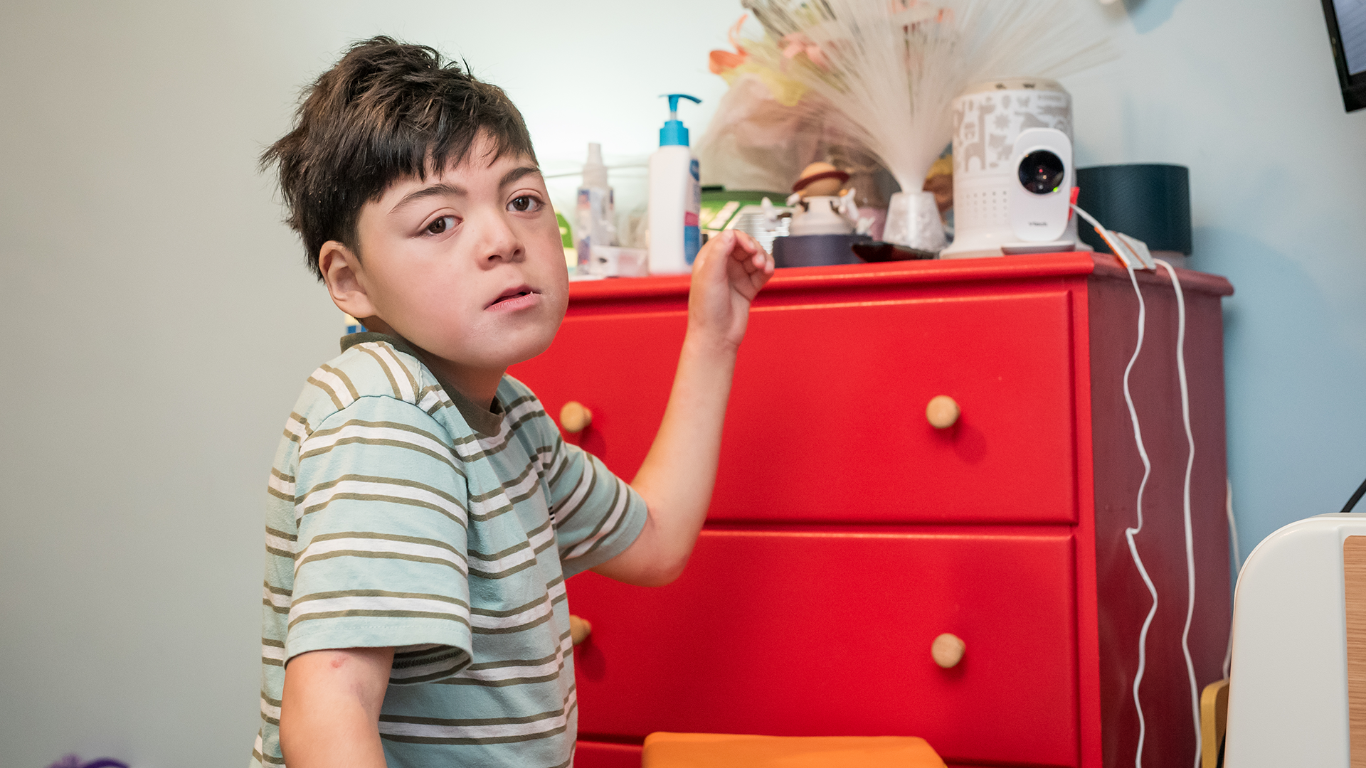 Thom standing beside a red dresser, reaching up toward items on top in a bedroom setting