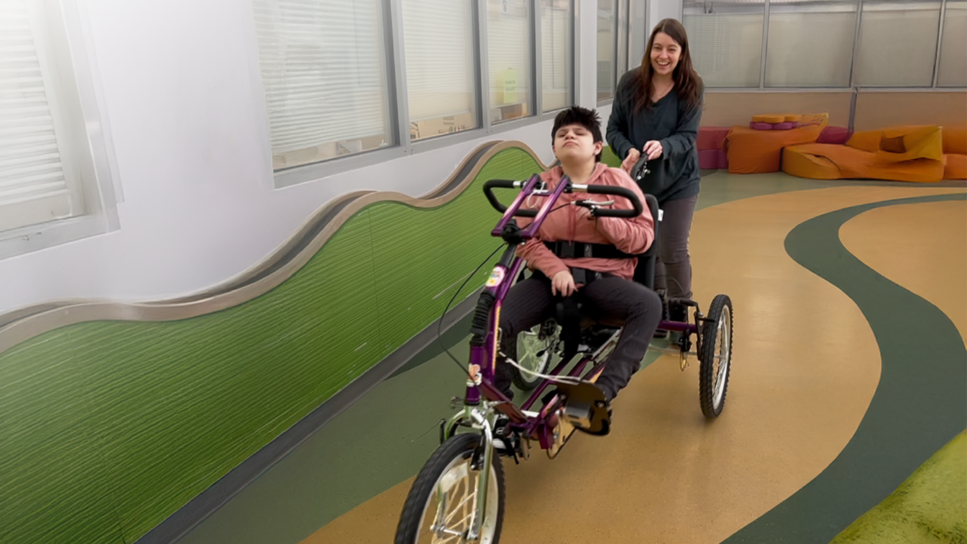 Girl riding adaptive bike while her mother steers from behind the bike